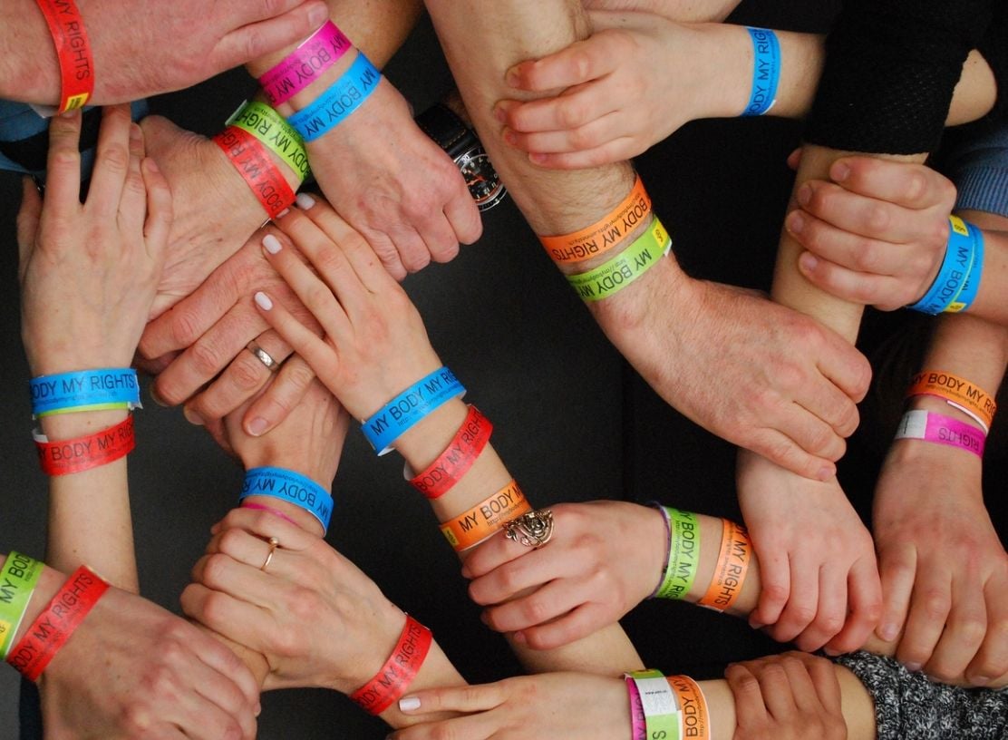 Bird's eye view of lots of hands holding wrists, in a connected, nice way. They're all wearing charity bands.