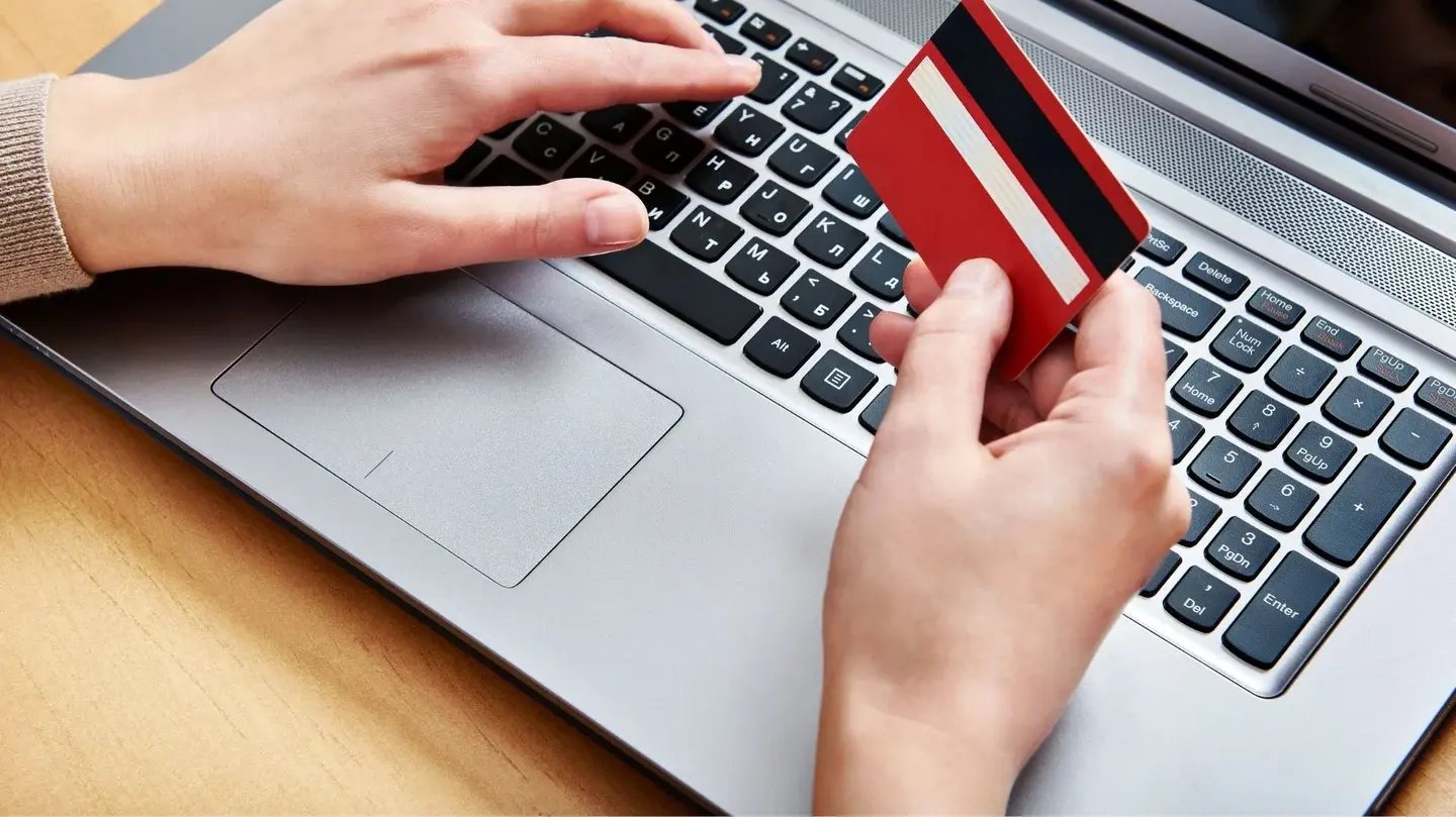 hands and a laptop. Right hand is holding a red credit card.