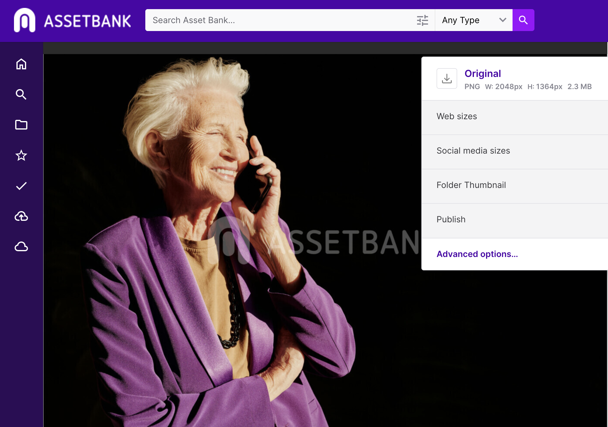 Photo of a glamorous grey haired lady talking on the phone. We can see her from the waist up. She is wearing a vivid purple suit jacket with a tan t-short underneath and large black beaded necklace. She looks stylish. She's smiling and the sun is lighting her as if it's golden hour. The background is completely dark; we can assume she is in a studio.